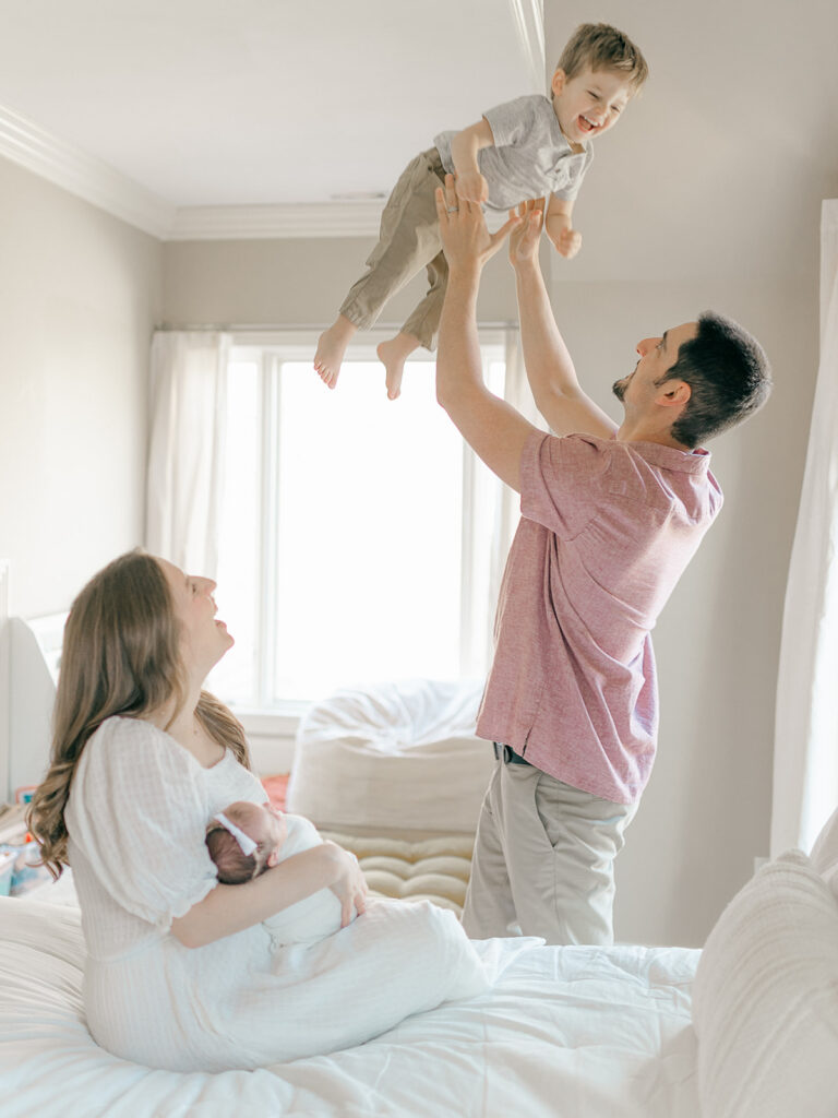 dad throwing up son while mom and newborn baby girl watch