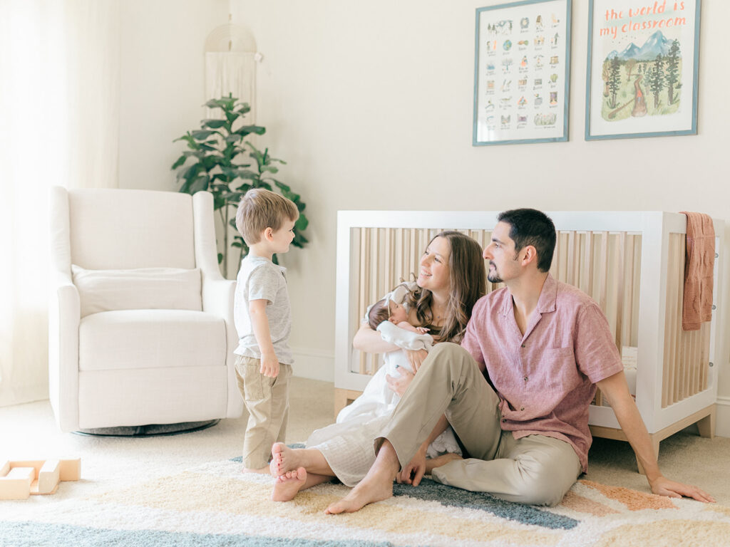 parents looking at toddler brother while holding newborn baby girl