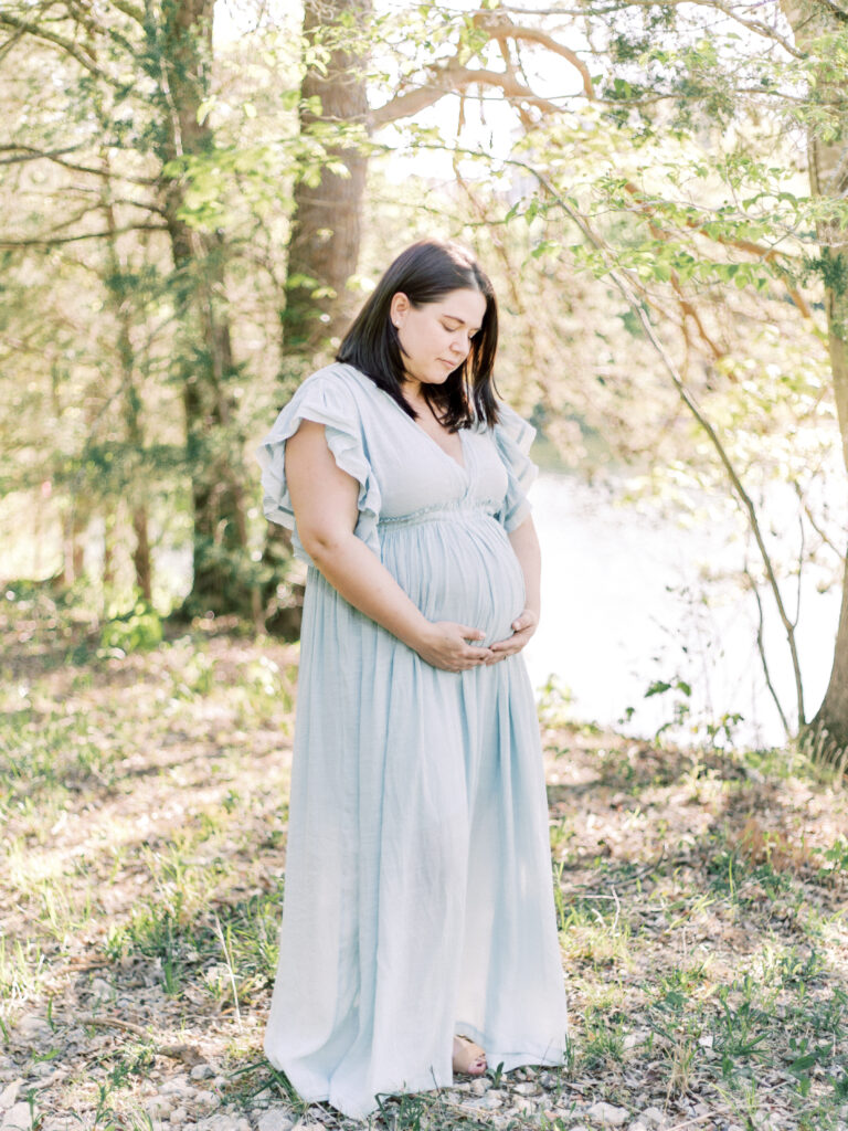 pregnant woman posing near pond admiring belly